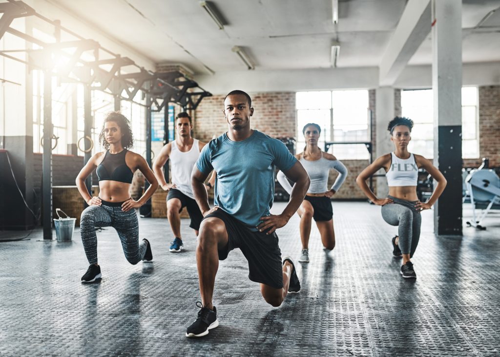 Shot of a group of young people doing lunges together during their workout in a gym.